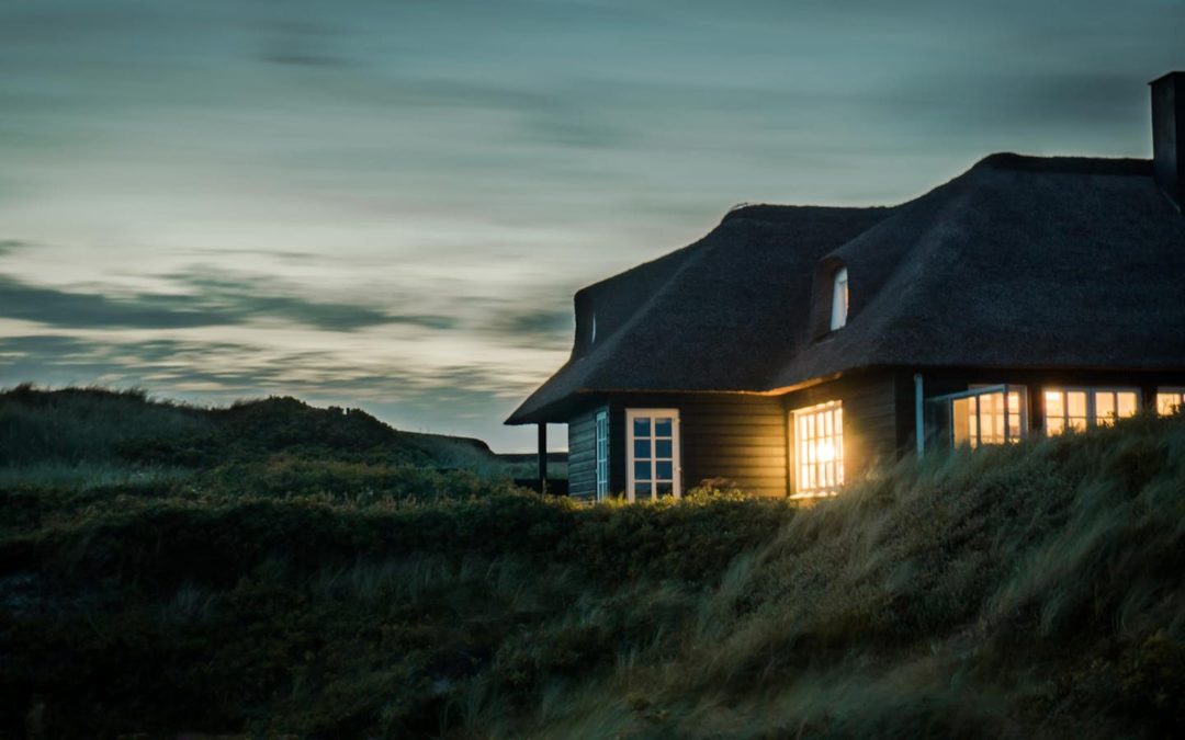 A scenic view of a cozy bungalow illuminated at dusk, nestled in lush greenery.